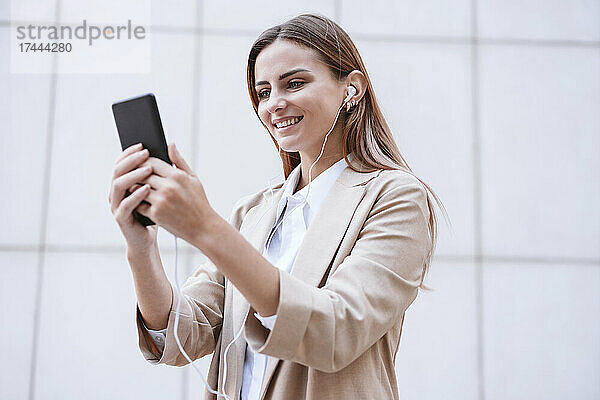 Geschäftsfrau lächelt  während sie einen Videoanruf über ihr Smartphone vor der Wand führt