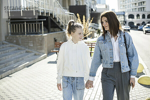 Mutter und Tochter halten Händchen beim Spaziergang auf der Stadtstraße