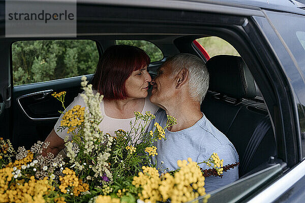 Romantisches älteres Paar sitzt mit Rainfarnblüten und küsst sich im Auto