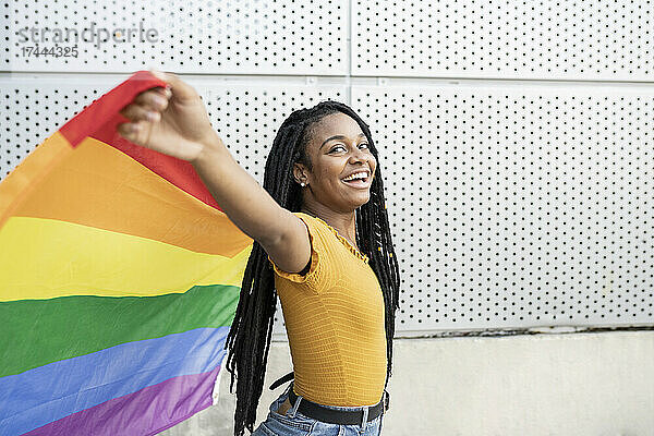 Glückliche lesbische Frau mit ausgestreckten Armen und Regenbogenfahne