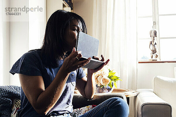 Frau mittleren Alters küsst digitales Tablet  während sie auf dem Sofa im Wohnzimmer sitzt