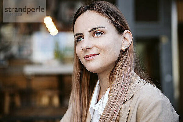 Lächelnde junge Geschäftsfrau mit blonden Haaren sitzt im Straßencafé