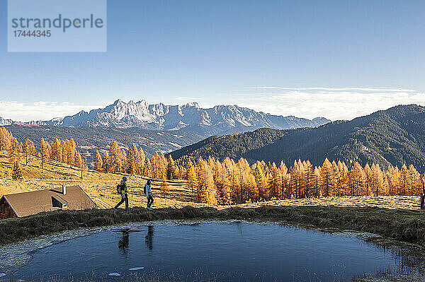 Zwei Wanderer wandern im Herbst an einem kleinen Teich in den Ennstaler Alpen vorbei