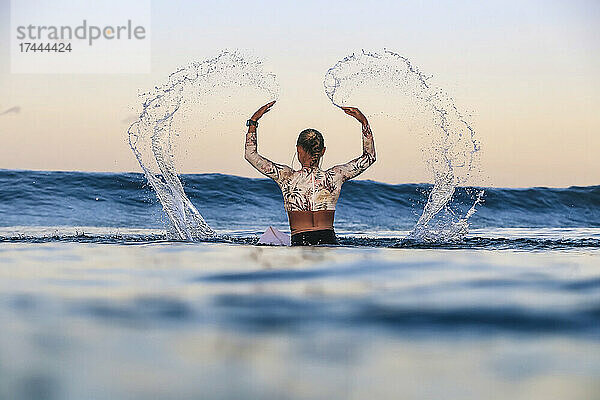 Female surfer splashing water in sea during sunset