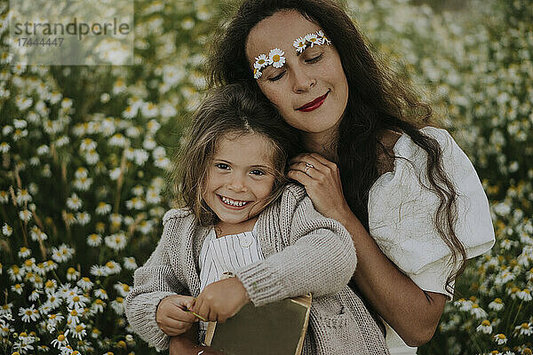 Mutter stützt sich auf lächelnde Tochter im Blumenfeld