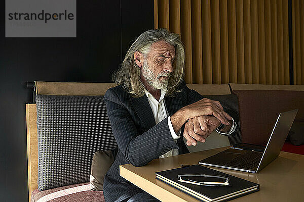 Geschäftsmann mit grauem Haar überprüft die Uhrzeit  während er im Hotelcafé sitzt
