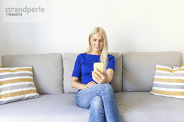 Frau macht Selfie mit dem Handy  während sie zu Hause auf dem Sofa sitzt