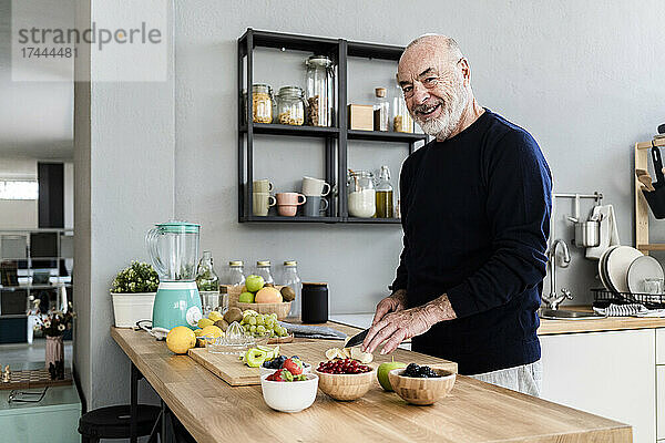 Lächelnder älterer Mann  der zu Hause in der Küche Früchte schneidet