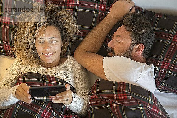 Lächelnde Frau benutzt Mobiltelefon von Mann im Bett
