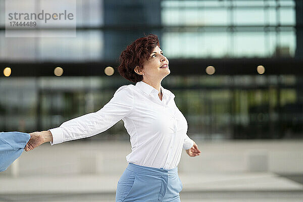 Berufstätige Frau mit kurzen Haaren tanzt vor dem Bürogebäude