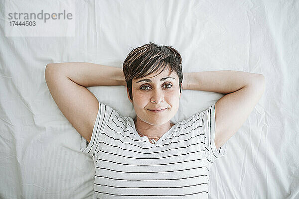 Frau mit den Händen hinter dem Kopf entspannt sich zu Hause im Bett