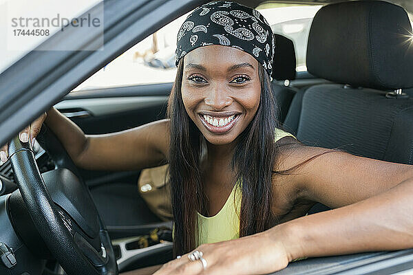 Fröhliche Frau mit Kopftuch sitzt im Auto