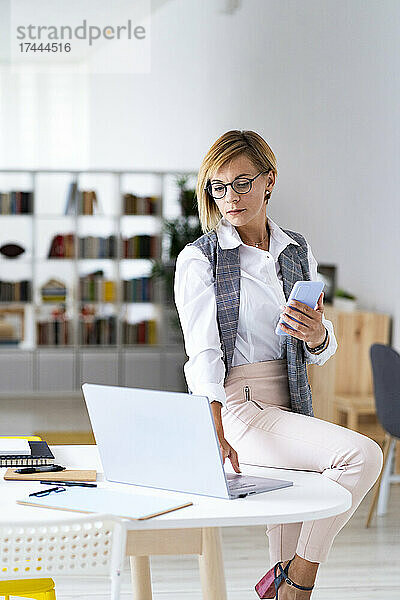 Eine berufstätige Frau im mittleren Erwachsenenalter benutzt einen Laptop  während sie im Büro am Schreibtisch sitzt