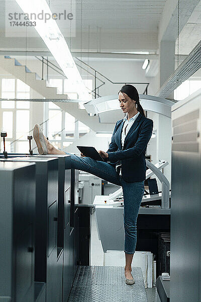 Geschäftsfrau streckt ihr Bein aus  während sie in der Industrie ein digitales Tablet nutzt