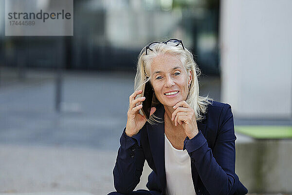Geschäftsfrau mit der Hand am Kinn  die auf dem Smartphone spricht