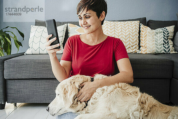 Frau benutzt Smartphone  während sie mit Golden Retriever zu Hause sitzt