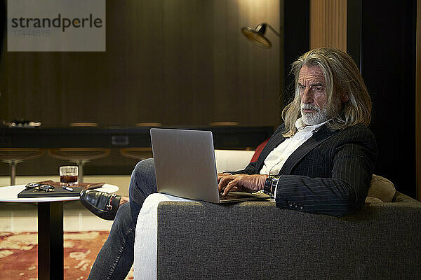 Geschäftsmann benutzt Laptop  während er auf dem Sofa im Hotel sitzt