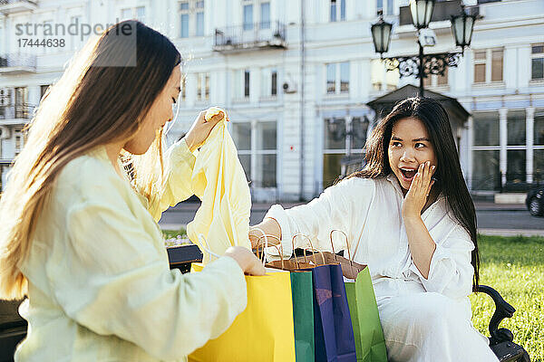 Überraschte Frau schaut einem Freund zu  der auf der Bank die Einkaufstasche überprüft
