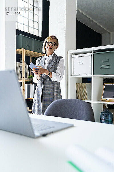 Lächelnde Geschäftsfrau mittleren Alters mit Mobiltelefon im Büro
