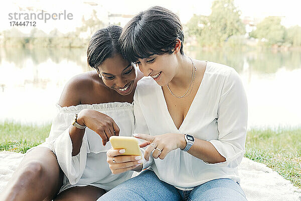 Glückliches lesbisches Paar  das am Seeufer sein Mobiltelefon teilt