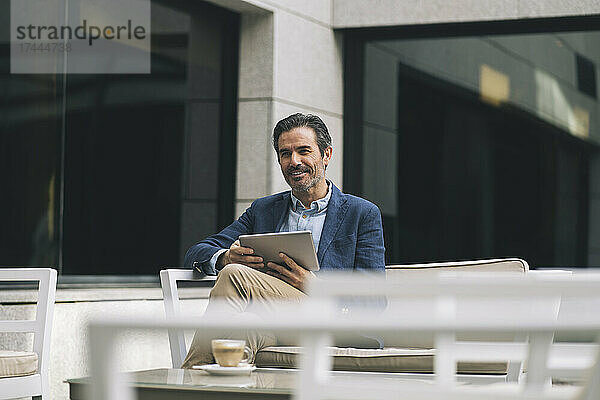 Lächelnder Geschäftsmann hält digitales Tablet im Hotel