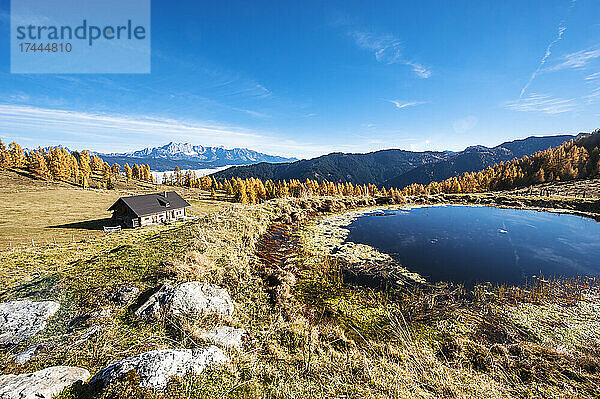 Abgeschiedene Hütte vor einem kleinen Alpensee im Herbst