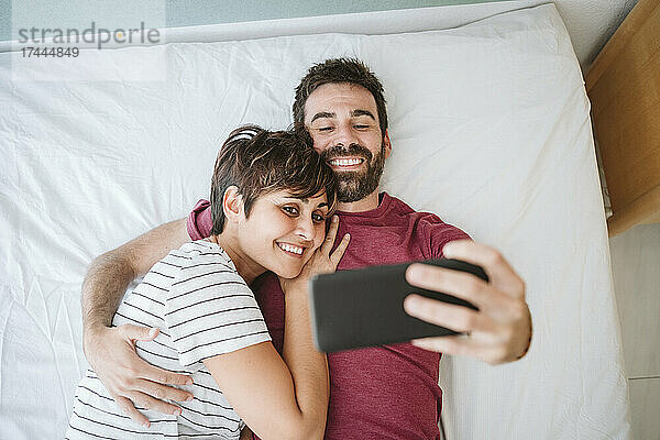 Mann und Frau machen ein Selfie über ihr Smartphone  während sie im Bett liegen