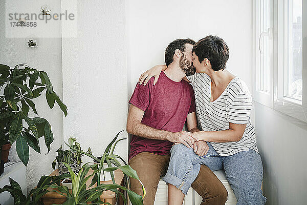 Mann und Frau küssen sich  während sie zu Hause neben Pflanzen sitzen