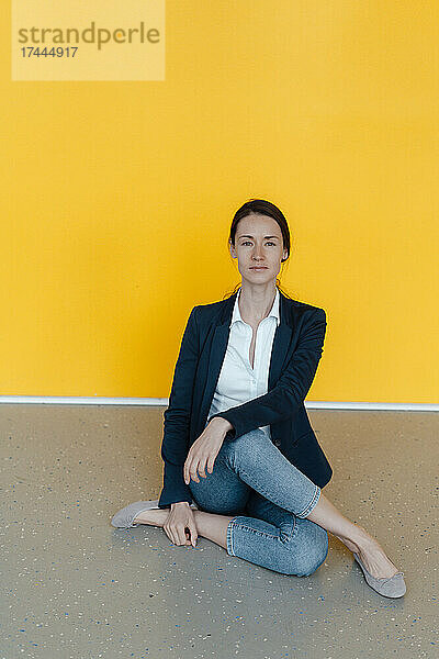 Geschäftsfrau praktiziert Yoga  während sie vor einer gelben Wand sitzt