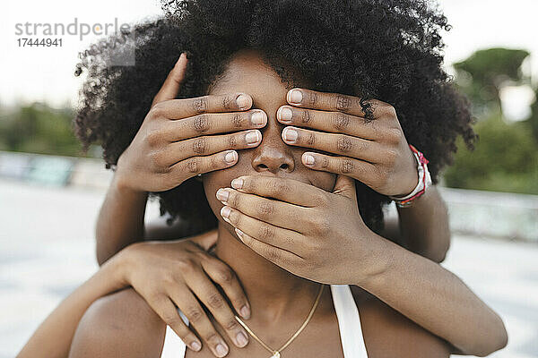 Junge Freundinnen bedecken Mund und Augen einer Afro-Frau