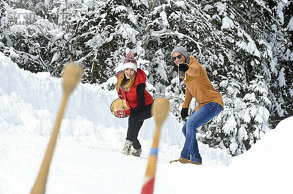 Lächelnder Mann gestikuliert mit seiner Freundin  die im Winter im Schnee spielt
