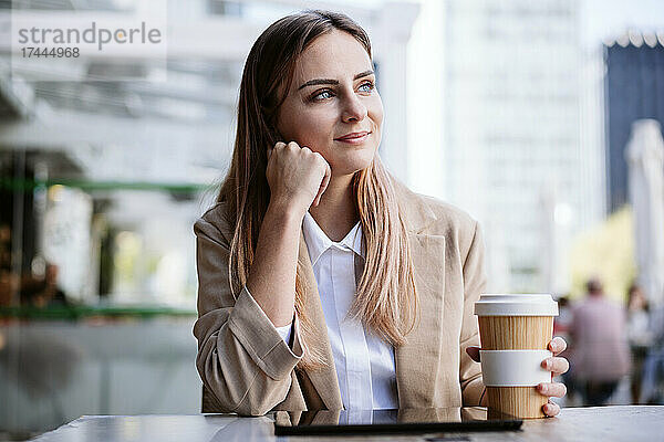 Nachdenkliche Geschäftsfrau mit Einwegkaffeetasse auf der Terrasse