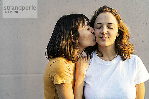 Frau mit geschlossenen Augen küsst ihre Freundin vor der Wand