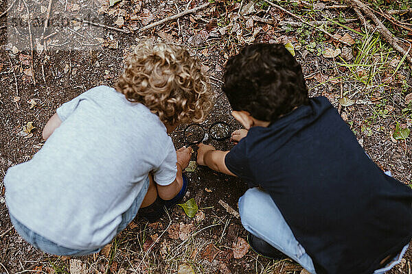 Jungen spielen mit Lupe  während sie im Wald hocken