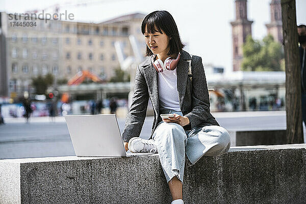 Geschäftsfrau benutzt Laptop  während sie auf Stützmauer sitzt