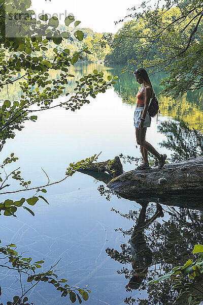 Wanderin steht auf einem umgestürzten Baum am Seeufer im Nationalpark Plitvicer Seen