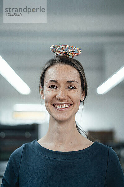 Glückliche Geschäftsfrau mit Drohne auf dem Kopf in der Werkstatt