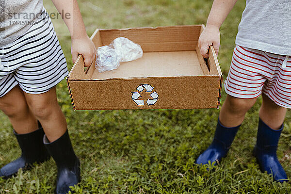 Jungen sammeln Plastik in einem Karton mit Recycling-Symbol