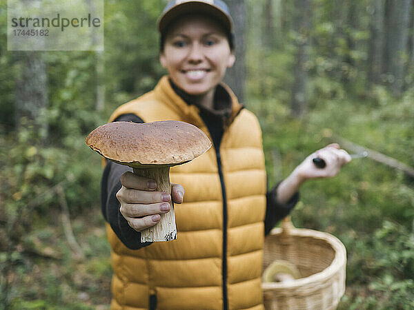 Lächelnde Frau hält Pilz im Wald