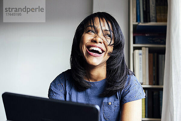 Frau mit digitalem Tablet lacht im Wohnzimmer