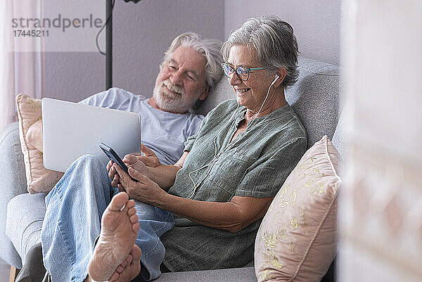 Lächelnder Mann mit Laptop und Frau  die auf dem Sofa im Wohnzimmer Musik hört