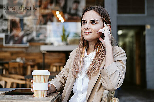 Nachdenkliche Geschäftsfrau mit Einwegbecher auf der Terrasse des Cafés