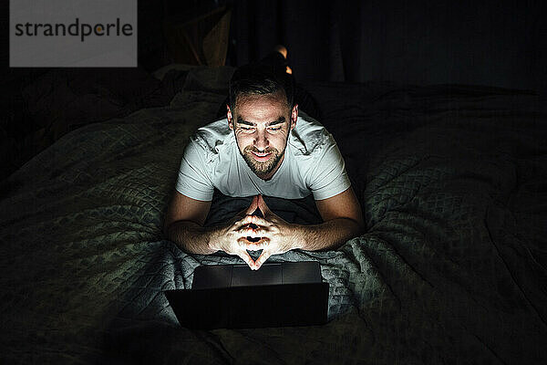 Lächelnder Mann gestikuliert während eines Videoanrufs über den Laptop im Bett