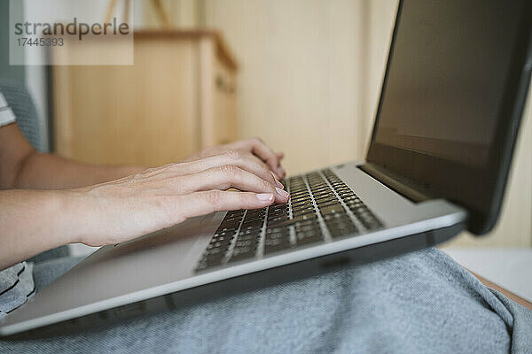 Frau tippt  während sie zu Hause einen Laptop benutzt
