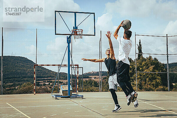 Männliche Freunde spielen an sonnigen Tagen Basketball auf dem Sportplatz