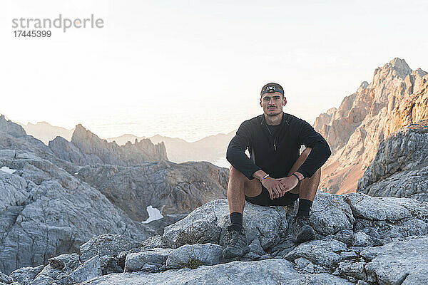 Junger männlicher Tourist sitzt auf einem Felsen  Picos de Europe  Kantabrien  Spanien