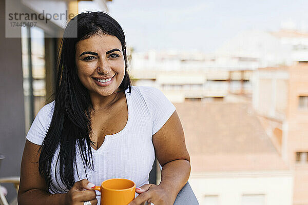 Lächelnde Frau trinkt Kaffee auf dem Balkon