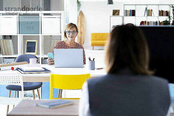 Geschäftsfrau mit Laptop schaut Kollegin im Büro an