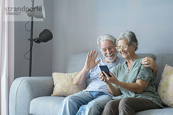 Lächelnder älterer Mann winkt während eines Videoanrufs einer Frau zu Hause