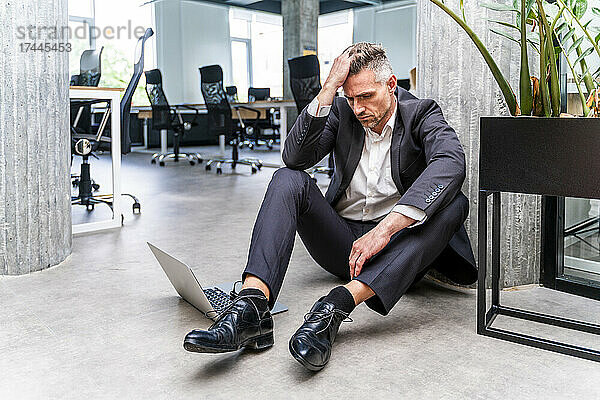 Besorgter Geschäftsmann mit Kopf in der Hand sitzt auf dem Boden im Büro